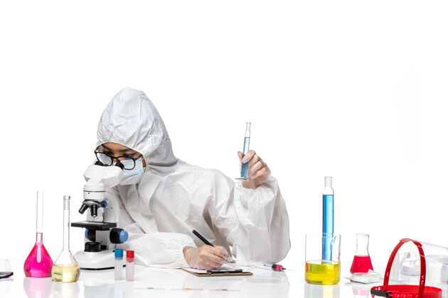 实验室正面图身穿特殊防护服的年轻女化学家拿着小烧瓶在白色背景的实验室里用显微镜观察化学病毒显微镜防护医生