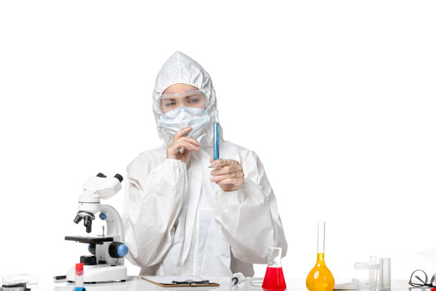 思考正面图年轻女医生穿着白色防护服带口罩因柯维德手持蓝色溶液思考白色背景飞溅病毒大流行柯维德-实验室外套套装面具
