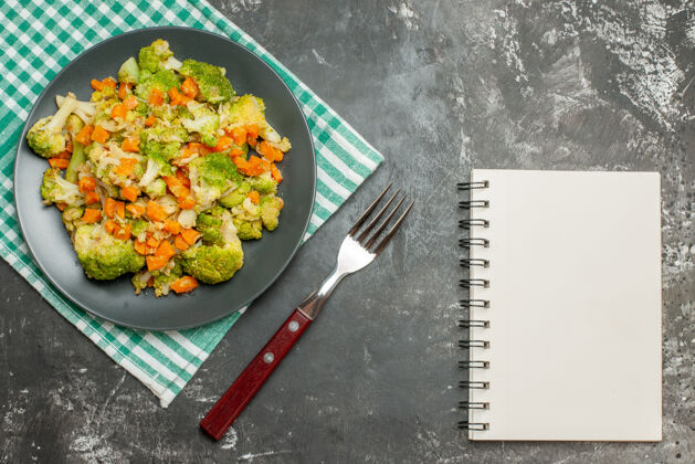 午餐绿色条状毛巾上的新鲜健康蔬菜沙拉和灰色桌子上的笔记本俯视图肉带菜新鲜
