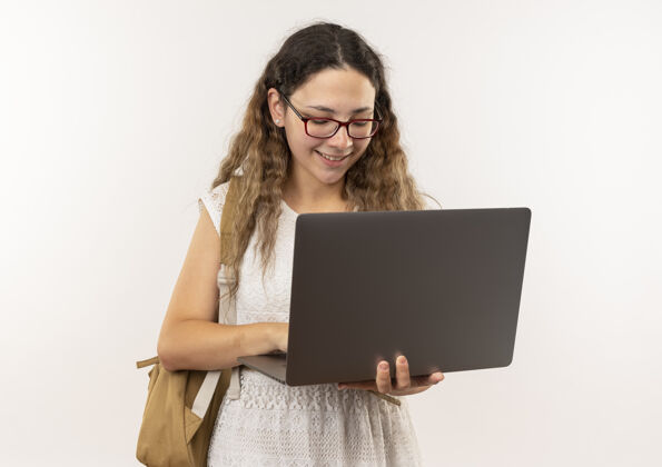 脸面带微笑的年轻漂亮的女学生戴着眼镜背着书包用笔记本电脑隔离在墙上市民微笑人