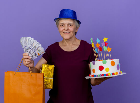 钱微笑的老妇人戴着聚会帽拿着钱礼盒纸购物袋帽子购物女人