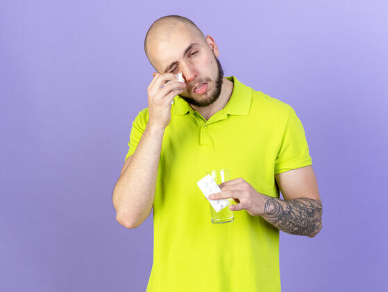 水苍白年轻的白人病人用纸巾擦鼻子拿着一杯水和一包紫色的药丸男人组织疾病