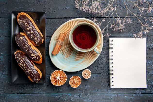 棕色俯视图：矩形板上的巧克力蛋糕一杯茶 柠檬和肉桂干 还有一本笔记本笔记本咖啡