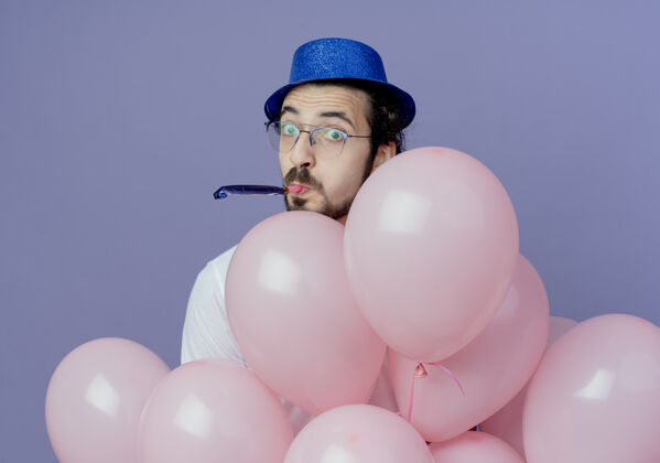 气球高兴的帅哥戴着眼镜和蓝帽子站在气球后面吹口哨男人眼镜请