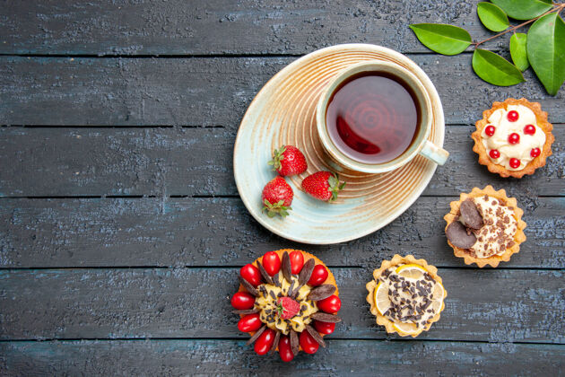 叶子俯视图一杯茶和草莓放在茶托上干橙子馅饼叶子和浆果蛋糕放在深色木桌的右边深色右边碗