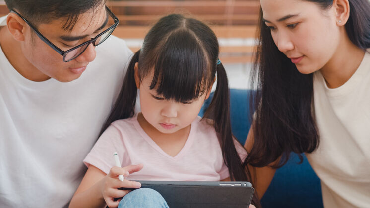 家庭快乐亚洲家庭爸爸 妈妈和女儿用电脑平板电脑技术坐在客厅的沙发上社会距离娱乐女人