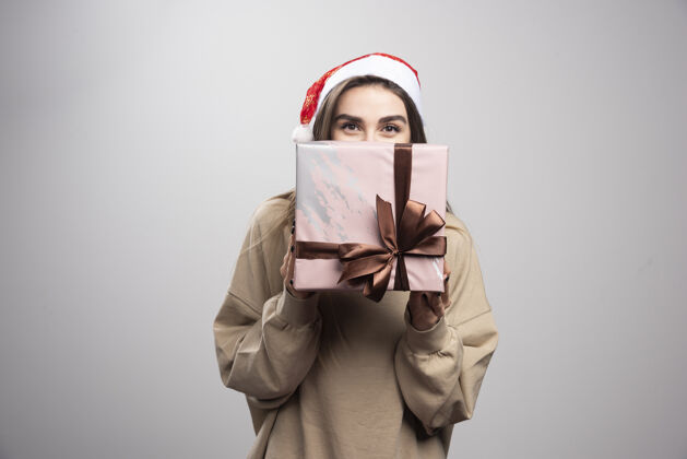 站着一个年轻女子用圣诞礼物遮住脸表情圣诞节女孩