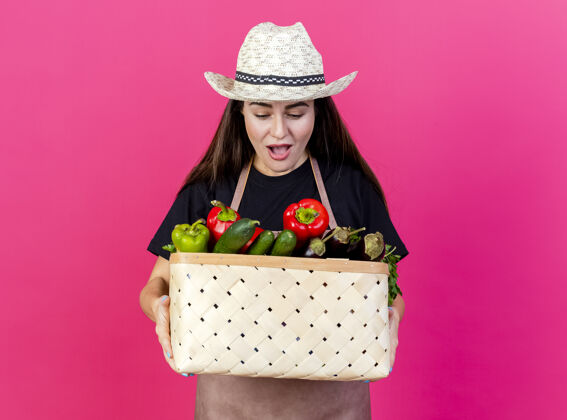 穿一个穿着制服的漂亮园丁女孩戴着园艺帽 拿着一只粉红色的菜篮 看着菜篮制服帽子篮子