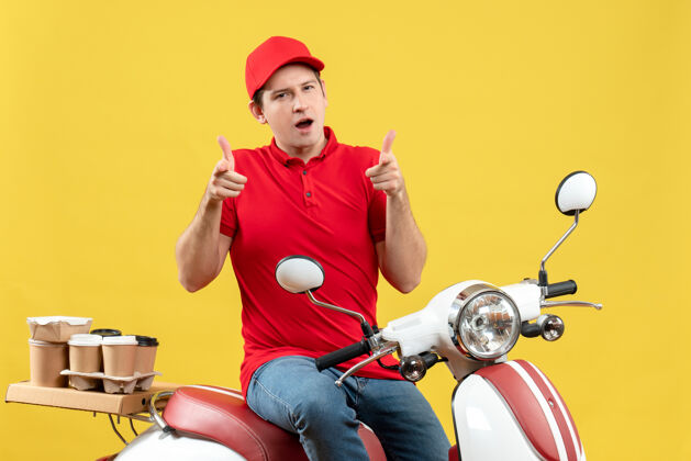 成人前视图困惑的年轻人穿着红色上衣 戴着帽子 在黄色的背景上向前传递命令命令健身运动