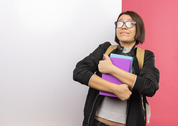 女孩高兴的年轻女学生戴着眼镜 背着书包站在白色的墙前 隔离在粉红色的墙上学生抱眼镜
