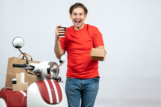 背景微笑着快乐的送货员穿着红色制服站在滑板车旁边 展示白色背景上的小盒子滑板车秀人