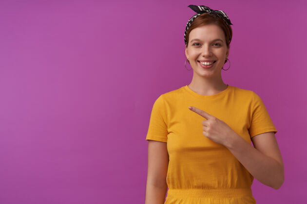 手指紫色墙壁上的女人穿着黄色t恤和黑色大手帕 情绪激动地微笑着 看着你开心的样子 把手指放在一边看着有趣的手指黑色衣服聊天