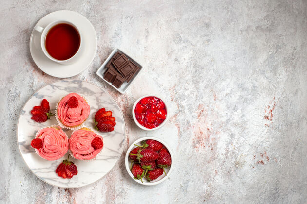 杯子粉红色草莓蛋糕的顶视图 白色表面上有奶油和一杯茶饼干奶油饼干