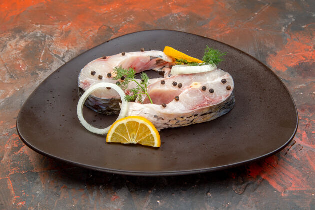 食物侧视图生鱼和胡椒柠檬片洋葱在一个黑色的盘子上混合颜色的表面美味生鱼一餐