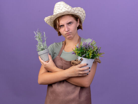 女性愤怒的年轻斯拉夫女园丁戴着园艺帽手持紫色花盆里的花朵花盆年轻园艺
