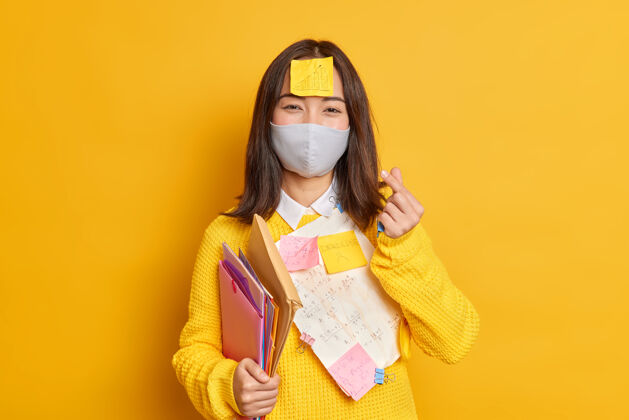 流行病高兴的女学生戴防护面具 以防止病毒和感染疾病的文件与书面必要的信息贴在衣服上使韩国人一样的标志爱单身黄色