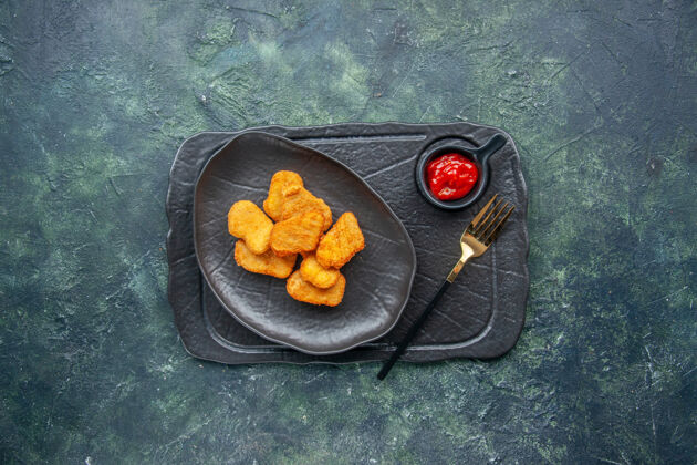 午餐黑色盘子上的鸡块和深色盘子上的叉子番茄酱的俯视图番茄酱盘子食物