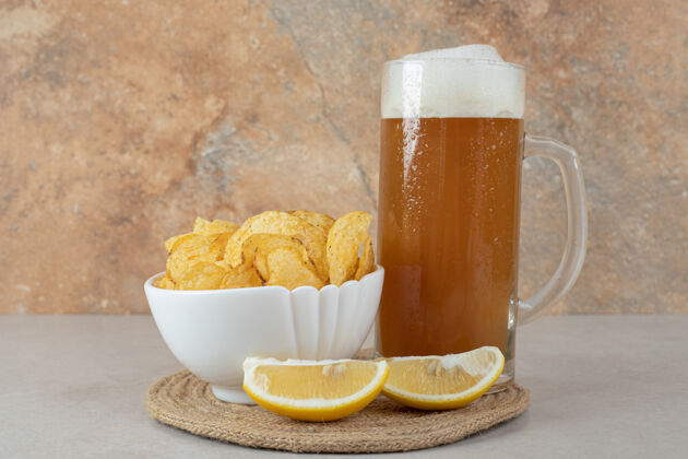 泡沫一杯柠檬片啤酒和一碗薯片放在石桌上水罐切片酒精