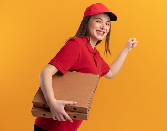 披萨微笑着的漂亮送货员 穿着制服 手里拿着拳头 手里拿着橘黄色的披萨盒保持制服橘子