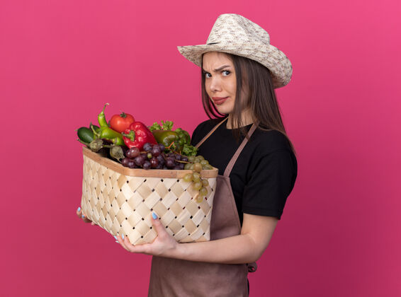 漂亮恼怒美丽的白人女园丁戴着园艺帽站在一旁拿着粉红色的菜篮子花园蔬菜篮子