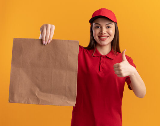 大拇指微笑着的漂亮送货员 穿着制服 竖起大拇指 手里拿着橘黄色的纸包制服女人抱着