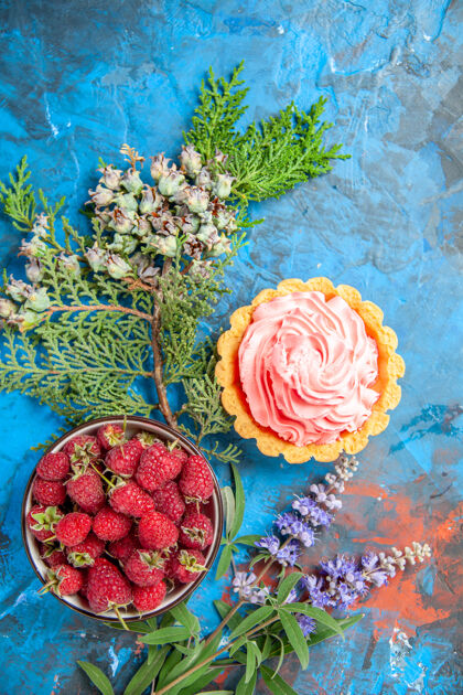鲜花蓝色表面上带有覆盆子的粉红色面团奶油碗的小馅饼俯视图覆盆子婚礼花束