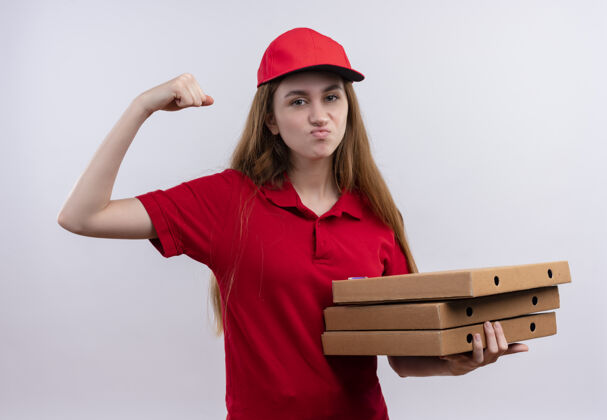 年轻穿着红色制服的自信的年轻送货女孩做着有力的手势 在孤立的空白处拿着包裹交付强大信心