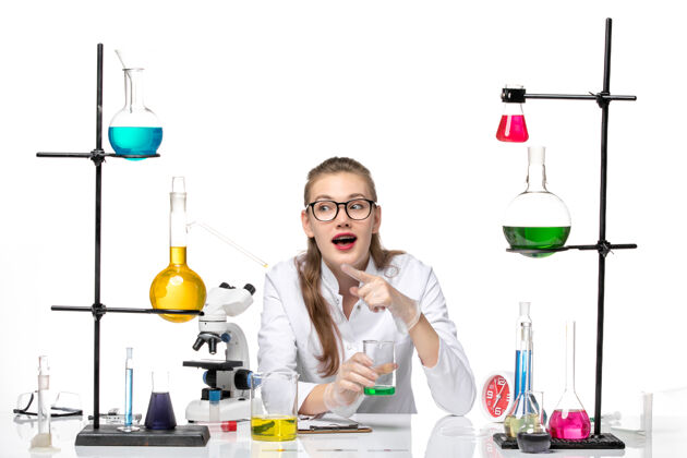 实验正面图身着医疗服的女化学家拿着白色桌子上的装有溶液的烧瓶化学大流行健康病毒烧瓶观察医学
