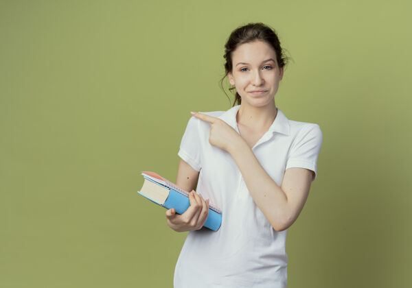 笔记高兴的年轻漂亮的女学生拿着书和便笺本在橄榄绿的背景和复印空间孤立的一面年轻垫绿色