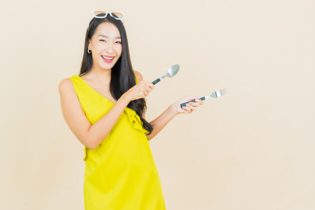 食物画像美丽的亚洲年轻女子在彩色墙上用勺子和叉子微笑情感女孩年轻