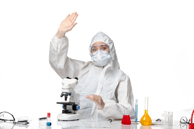 显微镜前视图：女医生穿着防护服 戴着口罩 在白色背景上挥舞着显微镜 病毒大流行 飞溅着病毒面具女医生飞溅
