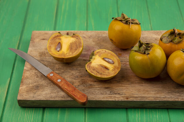 厨房有机柿子水果的俯视图在一个木制的厨房板上 在一张绿色的木桌上放着一把刀食品木材有机