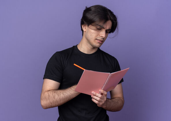 笔记本自信的年轻帅哥穿着黑色t恤在紫色墙上的笔记本上写着什么年轻小伙子自信