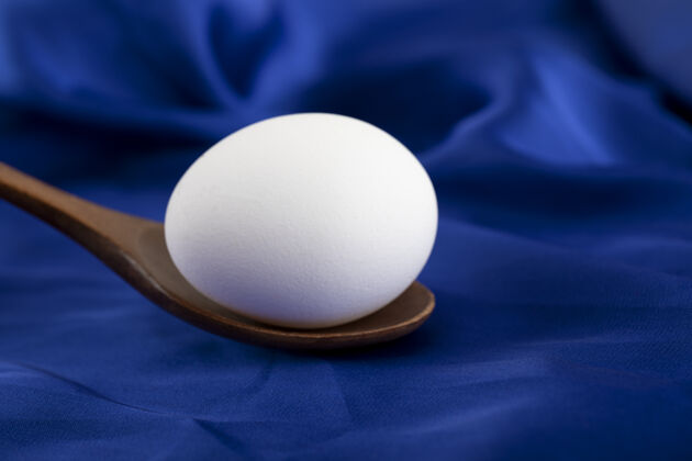 有机一个生鸡蛋 用木勺放在蓝色的棉布上勺子木头生的