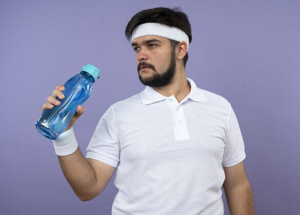 壁板年轻的运动型男子一边戴着头带 一边戴着手镯 手里拿着一个绿色的水瓶绿色水运动
