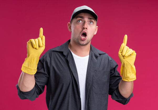 帽子令人印象深刻的年轻汉姆森清洁家伙穿着t恤衫 戴着手套点在粉红色的墙上孤立手套穿清洁