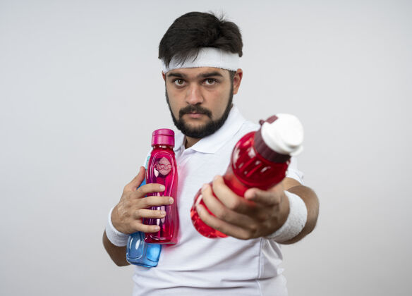 男人戴着头带和腕带的年轻运动型男子把水瓶孤立在白墙上穿运动奶瓶