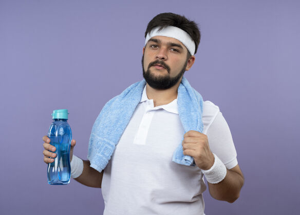 毛巾自信的年轻人戴着头带和腕带 肩上拿着毛巾拿着水瓶水头带人