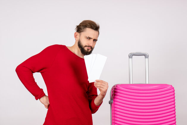 风景正面图：年轻男性 带着粉色包 手持机票 在白墙上航行 彩色旅行 旅游度假照片微笑机票年轻男性