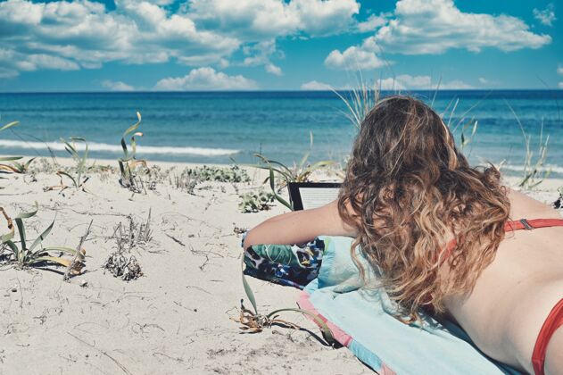 长一个留着长发 穿着红色比基尼的白人女人 躺在蓝海旁边的海滩上年轻海洋自然