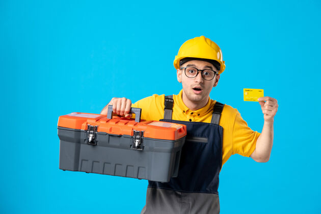 信贷正面图：穿着黄色制服的男工人 蓝色带工具箱和信用卡制服建筑商工具