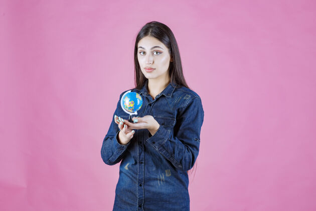 世界穿着牛仔夹克的女孩手心里拿着一个迷你地球仪装备地图学生