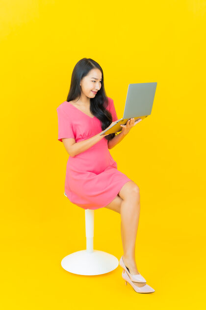 情绪画像美丽的亚洲年轻女子微笑着在黄色隔离墙上的电脑笔记本电脑微笑企业家快乐