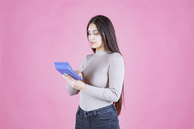 数学穿着灰色衬衫的女孩拿着一个蓝色的计算器 看着它 用它工作成人休闲收入