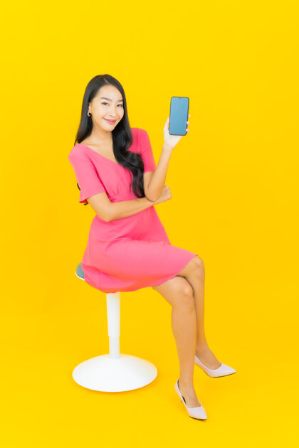 聪明画像美丽的亚洲年轻女子微笑着在黄色的墙上智能手机科技人物年轻