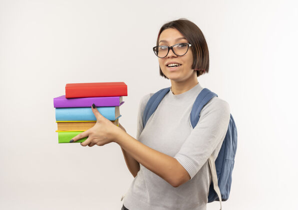 年轻快乐的年轻学生女孩戴着眼镜 背着书包 把书孤立在白色的地板上眼镜背戴