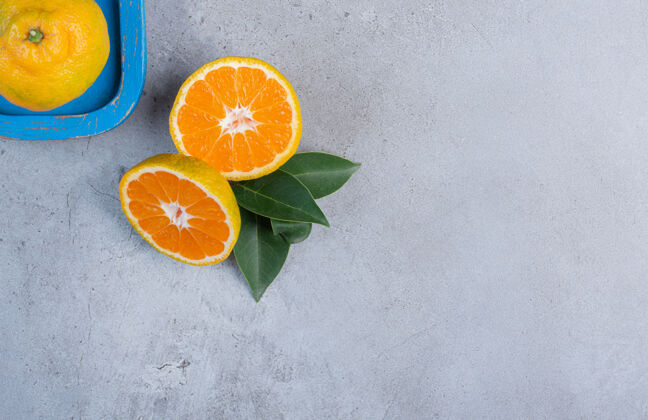 新鲜把一个橘子放在盘子里 旁边放着一片橘子叶 背景是大理石风味美味健康