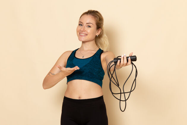 身体正面图穿着运动装的年轻女性手持跳绳站在浅白的墙上健康美容锻炼身体运动景观绳子健身