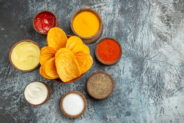 木材灰色桌子上放着不同香料 蛋黄酱和番茄酱的木质砧板上的脆片的水平视图服务可食用水果食品