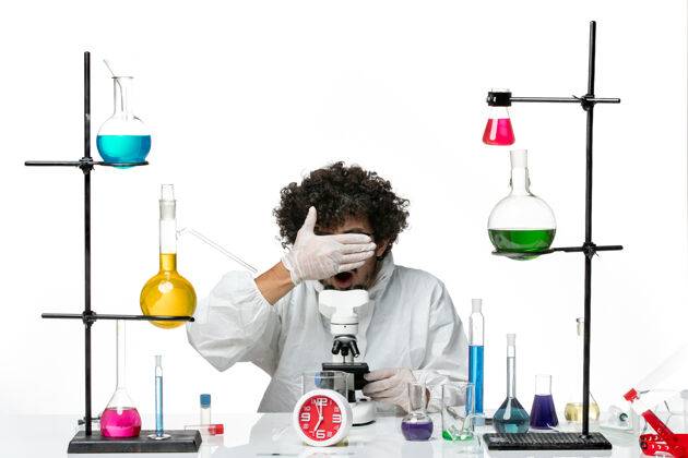 专用正面图穿着白色特别套装的年轻男科学家正在尝试使用显微镜容器实验烧杯